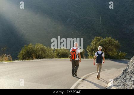 due uomini con zaini, uomo maturo 60 anni e uomo 30 anni, zaino in spalla a panama che cammina lungo la strada con un magnifico paesaggio naturale, guardando Foto Stock