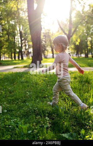 Bambini felici che camminano nel parco al tramonto. Erba verde e foglie, aria fresca che cammina. Bambino sano andare in natura, gioco attivo. Bokeh leggero e soffice. Foto Stock