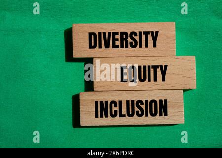 Parole di diversità, equità e inclusione scritte su un blocco di legno con sfondo verde. Diversità concettuale, equità e inclusione DEI simboli. Copia spazio Foto Stock