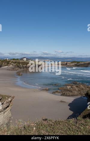 Una spiaggia panoramica con coste rocciose, cieli azzurri e dolci onde, che offrono un'atmosfera tranquilla e serena Foto Stock