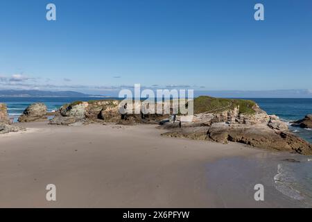 Una spiaggia tranquilla con formazioni rocciose, cieli azzurri e acque calme, che evocano un senso di tranquillità e bellezza naturale Foto Stock