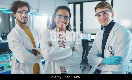 Laboratorio di scienze mediche con team di tre giovani scienziati di successo. Bella donna nera, bella latina e caucasica maschi gli scienziati sorridono mentre guardano la fotocamera. Scatto verticale medio Foto Stock