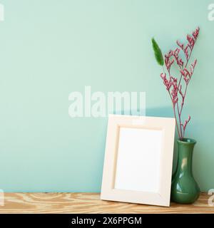 Cornice fotografica in legno e vaso di fiori secchi su scaffale in legno. sfondo muro menta Foto Stock