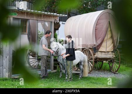 Adorf, Germania. 16 maggio 2024. L'agricoltore biologico Bert Bochmann si trova con il suo pony Eddie e Jane Bochmann accanto a un vecchio carro trainato da cavalli pieno di fieno, che serve come luogo di riposo per i pellegrini. La fattoria si trova su un sentiero medievale che collega il monastero di Chemnitz, che ora fa parte della via sassone di San Giacomo. L'offerta per gli escursionisti in cerca di illuminazione deve essere ampliata. Tra un anno, le abitazioni portatili per i pellegrini potrebbero trovarsi nei prati di Erzgebirge tra mucche e cavalli. Crediti: Jan Woitas/dpa/Alamy Live News Foto Stock