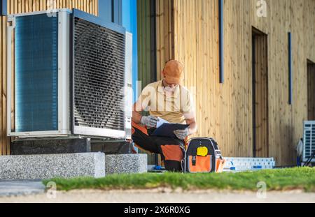 Tecnico HVAC che lavora su una moderna pompa di calore di fronte a un edificio. Foto Stock