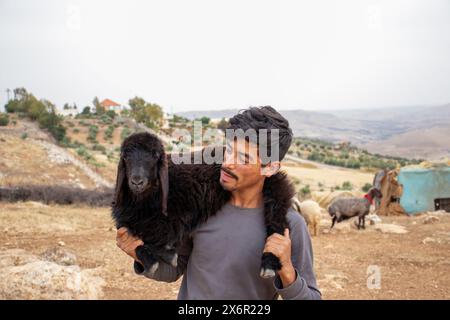 Giovane adolescente arabo che tiene piccole pecore che si sente felice e ringrazia Dio per i suoi doni nel deserto Foto Stock