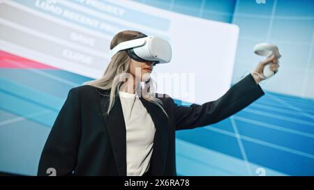 Interior Designer Making presentazione di un moderno software di realtà virtuale per la progettazione di spazi abitativi. Un ingegnere donna utilizza la cuffia e i controller per mostrare le funzionalità su un grande schermo sul palco. Foto Stock