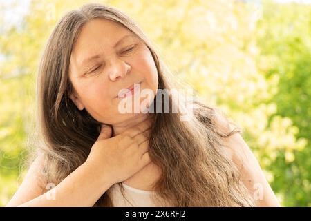 Primo piano collo femminile maturo, paziente che tiene in mano l'area interessata, sperimentando dolore alla gola, preoccupazione per la salute, varie cause, tonsillite Foto Stock