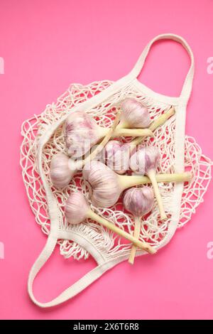 Borsa a cordoncino con teste d'aglio su sfondo rosa brillante, vista dall'alto Foto Stock