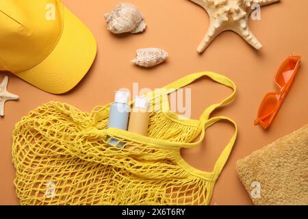 Borsa con cordoncino e diversi accessori da spiaggia su sfondo arancione pallido, piatto Foto Stock