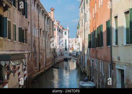 Uno dei tanti piccoli e graziosi ponti pedonali su un canale di Venezia, in Italia, ombreggiato da alti edifici su entrambi i lati Foto Stock