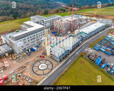 Ampio cantiere in un ambiente rurale con diversi edifici in costruzione, gru alte e una strada, nuovo ospedale cantiere Foto Stock