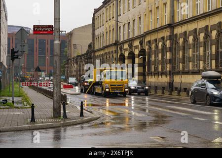 Wroclaw, Polonia - 4 agosto 2023: Un carro attrezzi sta evacuando un'auto in avaria in una giornata di pioggia in un'area urbana del centro. Numerosi veicoli sono guidati dal Foto Stock