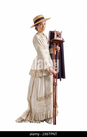 Giovane donna con fotocamera che indossa un abito beige vintage anni '1880 e un cappello di paglia isolato sul bianco Foto Stock