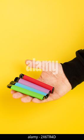 Sigarette elettroniche usa e getta di diversi gusti in mano su sfondo giallo. Il concetto di fumo moderno, vaping e nicotina Foto Stock