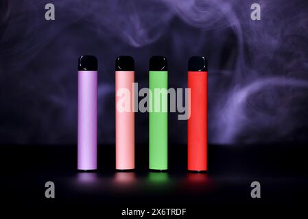 Set di sigarette elettroniche monouso colorate su sfondo nero con fumo colorato. Il concetto di fumo moderno, vaping e nicotina Foto Stock