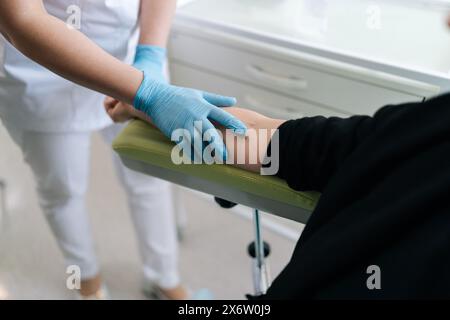 Dettaglio ritagliato di venature irriconoscibili sul braccio del paziente seduto su una comoda poltrona in una clinica moderna con interni bianchi e moderni Foto Stock