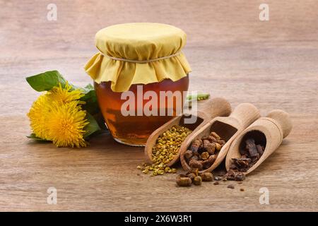 Un barattolo di miele con coperchio in tessuto, granuli di polline, beebread e fiori di dente di leone Foto Stock