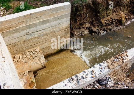 Un tombino sotto la strada con un torrente che scorre attraverso di essa Foto Stock