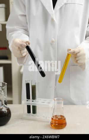 Operaio di laboratorio che tiene in mano provette con diversi tipi di olio grezzo su un tavolo di marmo chiaro, primo piano Foto Stock