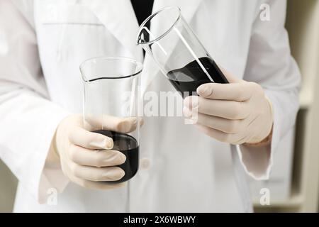 Operaio di laboratorio che versa olio grezzo nero nel becher al chiuso, primo piano Foto Stock