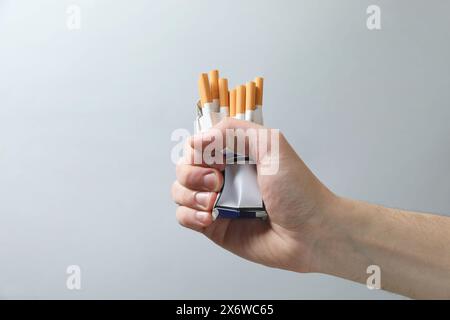 Basta fumare. Uomo che regge un pacchetto con sigarette su sfondo grigio, primo piano Foto Stock