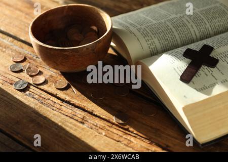 Dona e dai un concetto. Ciotola con monete, croce e Bibbia su un tavolo di legno Foto Stock