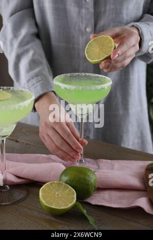 Donna che spreme il succo di lime nel bicchiere con un delizioso cocktail Margarita al tavolo di legno, primo piano Foto Stock