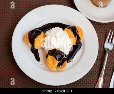 C'è un dessert sul piatto - diversi profiterole e panna montata decorata sotto forma di piccole palle. Foto Stock