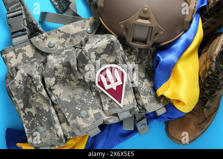 Giubbotto di scarico con stemma militare dell'esercito ucraino, bandiera Ucraina, stivali e casco tattico su sfondo blu Foto Stock