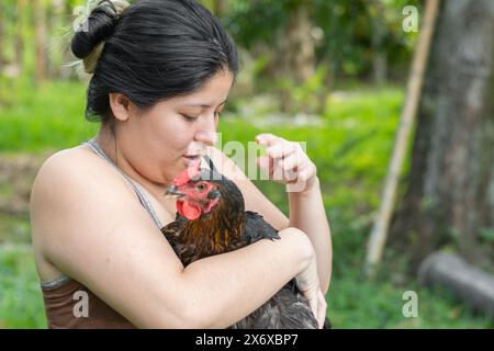 una donna latina che tiene una gallina tra le braccia, cercando di evitare che scappi Foto Stock