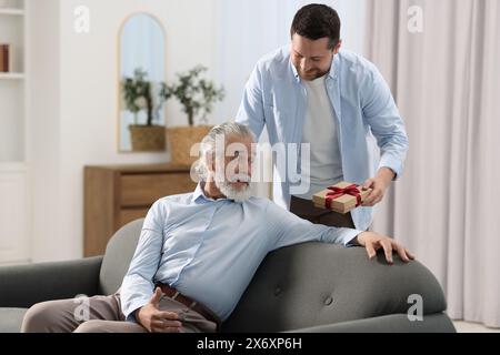 Figlio che regala una confezione regalo a suo padre a casa Foto Stock
