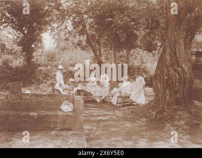 Un tavolo fisso ai tropici con gente europea vestita di bianco., Batuwan vicino a Soemenep 1910 (titolo su oggetto), Photographies (titolo della serie), gli uomini indossano uniformi tropicali bianche, un uomo con un casco da pith, altri due uomini indossano un cappello di paglia, le donne indossano abiti bianchi o gonne batik con un gilet bianco. Foto dall'album "Photographies"., fotografia, Frits Freerks Fontein Fz., (attribuito a), Frits Freerks Fontein Fz., (attribuito a), Madura, (forse), Paesi Bassi, (possibile), c. 1910, cartone, altezza, 79 mm x larghezza, 109 mm, altezza, 242 mm x larghezza, 333 mm Foto Stock