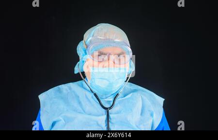 Personale medico. Ritratto di un medico serio in maschera protettiva, occhiali e cappuccio chirurgico monouso con stetoscopio. Operaio ospedaliero in uniforme medica Foto Stock