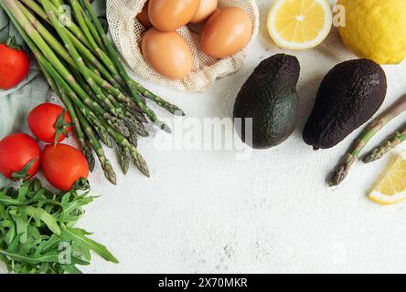 Una varietà di verdure fresche, tra cui asparagi, pomodori e rucola, sono ordinatamente organizzati accanto a avocado maturi e un sacchetto di uova scure. L'arr Foto Stock