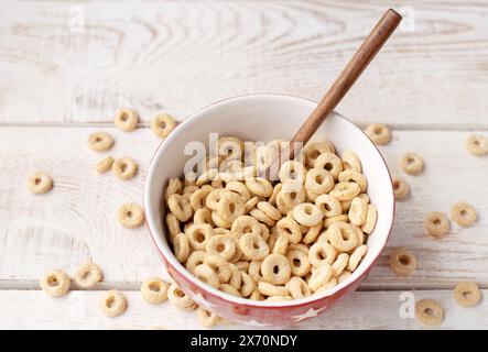 sani anelli di cereali su uno sfondo di legno chiaro in un piatto e sparsi sul tavolo. mattina, mangia. Colazione sana per bambini. Muesli secchi Foto Stock