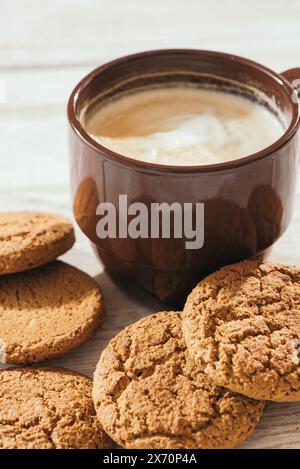 Una tazza di caffè aromatico con biscotti d'avena. Latte per colazione in una bella tazza marrone. Sfondo in legno. Primo piano. Foto Stock