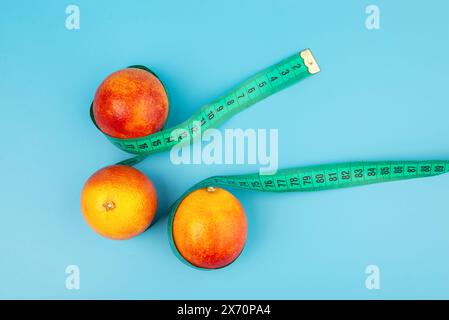 Un mandarino rosso-arancione avvolto in un metro a nastro su sfondo azzurro. dieta e concetto di cibo sano. Arancia sanguinosa. Vista dall'alto. Foto Stock