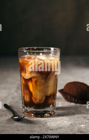 Caffè ghiacciato in un alto bicchiere ricoperto di panna e biscotti con gocce di cioccolato su un tavolo rustico grigio. Drink estivo freddo su sfondo scuro Foto Stock