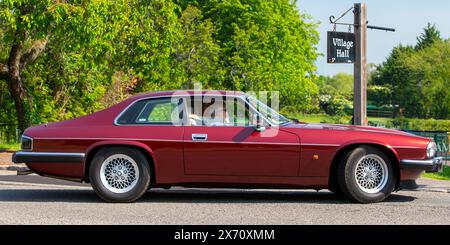 Stoke Goldington, Regno Unito - 11 maggio 2024: Auto d'epoca Jaguar XJS maroon 1994 che viaggia attraverso un villaggio inglese Foto Stock