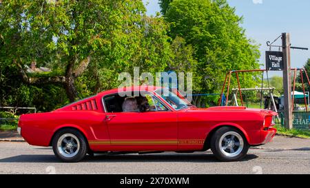 Stoke Goldington, Regno Unito - 11 maggio 2024: Auto d'epoca Ford Mustang rossa 1965 che viaggia attraverso un villaggio inglese Foto Stock