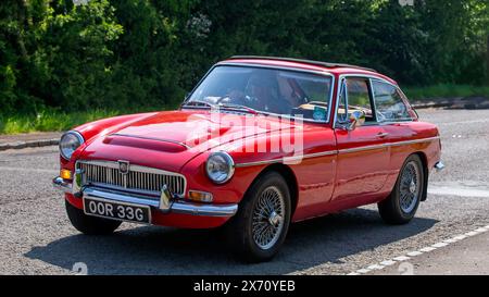 Stoke Goldington, Regno Unito - 11 maggio 2024: `1968 auto rossa MGC GT che guida su una strada britannica Foto Stock