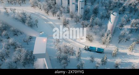 Un camion con un dispositivo di riempimento dell'idrogeno, serbatoi di stoccaggio dell'idrogeno e un parco eolico catturati da una vista a volo d'uccello nel mezzo di una foresta innevata. 3D Ren Foto Stock