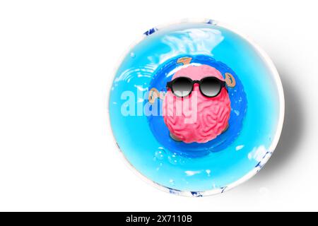 Piscina immersa in una tazza di caffè, dove un cervello umano, indossando occhiali da sole, galleggia piacevolmente su un anello gonfiabile. Tempo libero, creatività e reju mentale Foto Stock