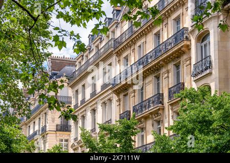 Facciate di edifici residenziali in classico stile Haussmannien parigino costruiti lungo un viale alberato. Concetto di mercato immobiliare residenziale Foto Stock