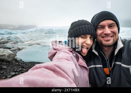 Divertente coppia viaggiante che scatta fotografie autoritratti sull'Islanda divertendosi durante il viaggio dalla laguna glaciale di Jokulsarlon/lago glaciale. Turisti che si divertono Foto Stock