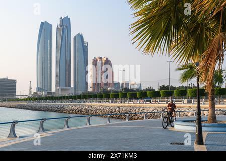 Abu Dhabi, Emirati Arabi Uniti - 4 gennaio 2024: Un ciclista gode di una giornata di sole sulla Corniche con grattacieli maestosi sullo sfondo. Foto Stock