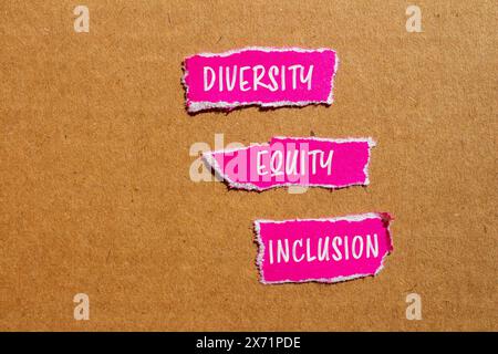 Parole di diversità, equità e inclusione scritte su pezzi di carta rosa strappati con sfondo in cartone. Diversità concettuale, equità e inclusione DEI sy Foto Stock