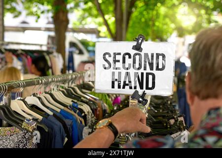 17 maggio 2024: L'uomo guarda i vestiti in un mercato delle pulci. Il cartello sopra gli abiti di seconda mano recita: Seconda mano. FOTOMONTAGGIO *** Mann schaut sich Kleidung auf einem Flohmarkt AN. Auf dem Schild über den gebrauchten Klamotten der Schriftzug: Seconda mano. FOTOMONTAGE Foto Stock