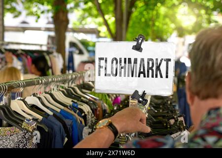 17 maggio 2024: Cartello: Mercato delle pulci, sopra un appendiabiti dove un uomo guarda merci usate. FOTOMONTAGGIO *** figlio: Flohmarkt, über einem Kleiderständer an dem ein Mann gebrauchte Waren anschaut. FOTOMONTAGE Foto Stock